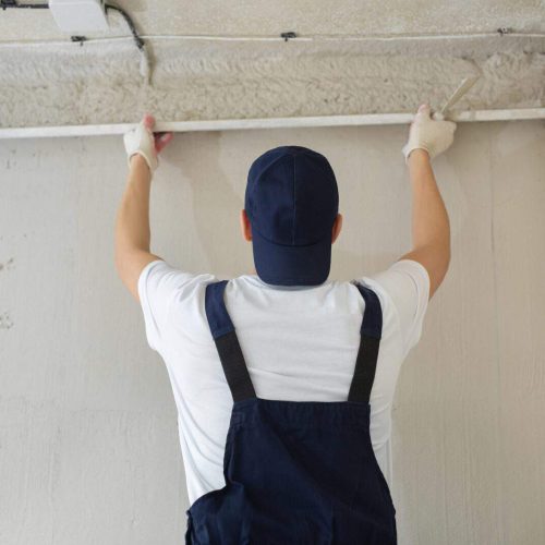 A young man, a plasterer, a builder, holds a metal ruler and aligns a freshly plastered wall.