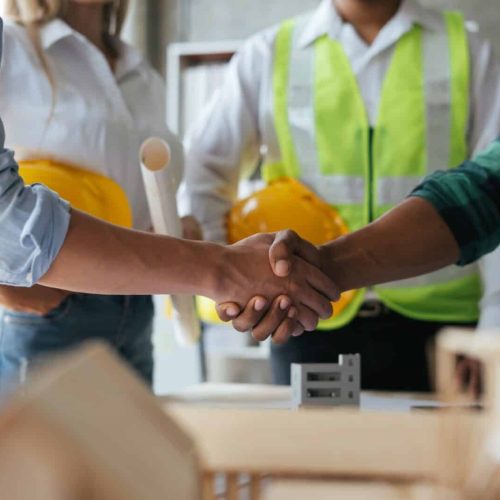 Construction workers, architects and engineers shake hands after completing an agreement in an offic