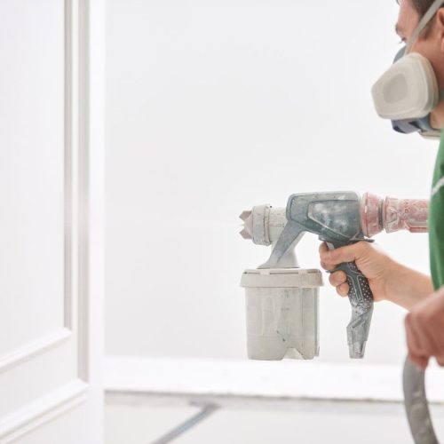 Worker painting wall with spray gun in white color.